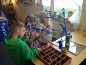 Children wrapping tissue paper around branches of a tree and decorating them with pieces from nature
