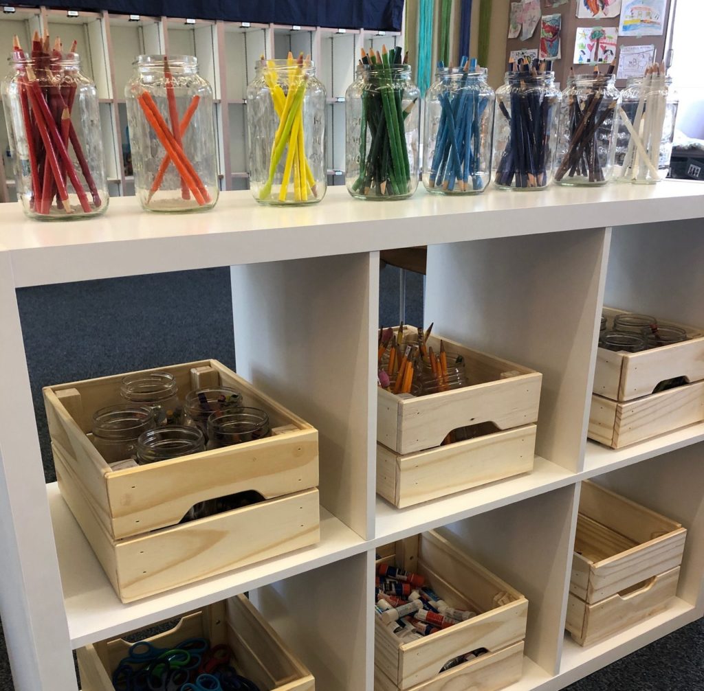 White open shelves with wooden boxes and jars of colored pencils for students